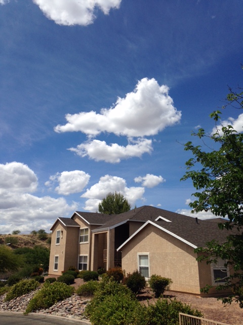 Two-story apartment buildings above landscaped slopes beneath a partly cloudy sky.